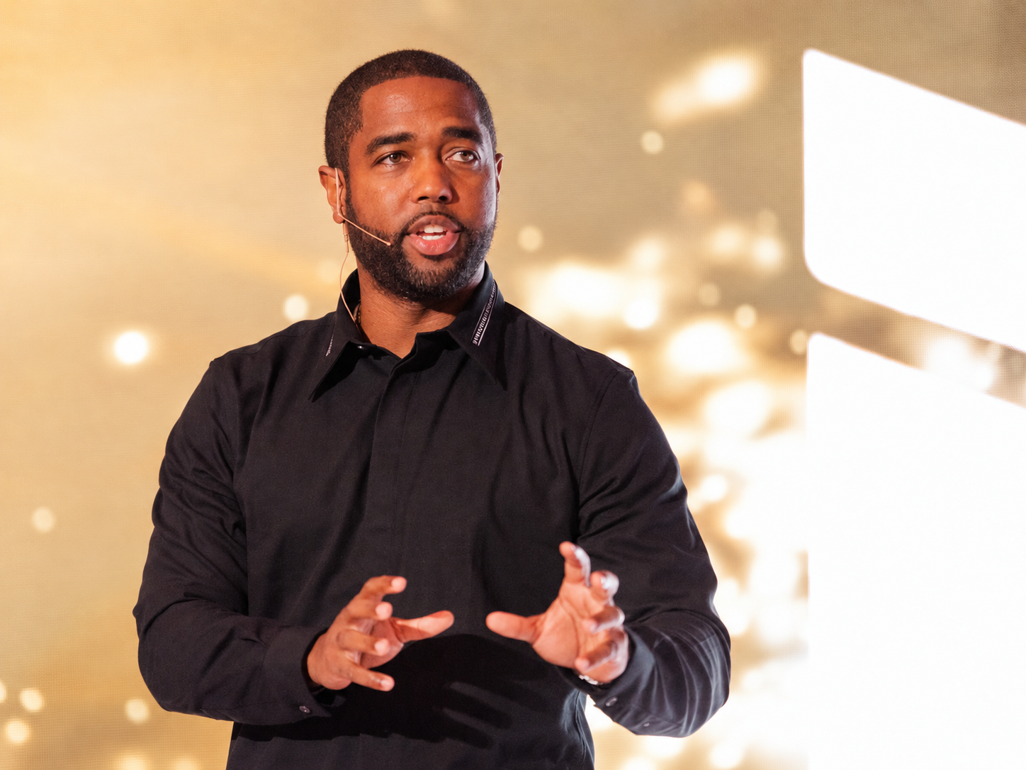 Tony A. Gaskins Jr. speaking on stage in front of a champagne gold LED backdrop