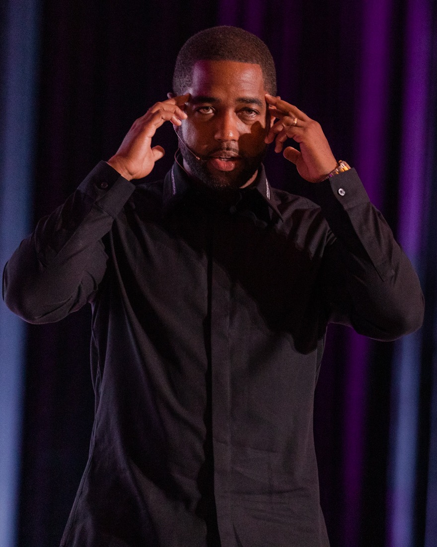 Tony A. Gaskins Jr. speaking on stage in a black shirt, hands raised mid-message
