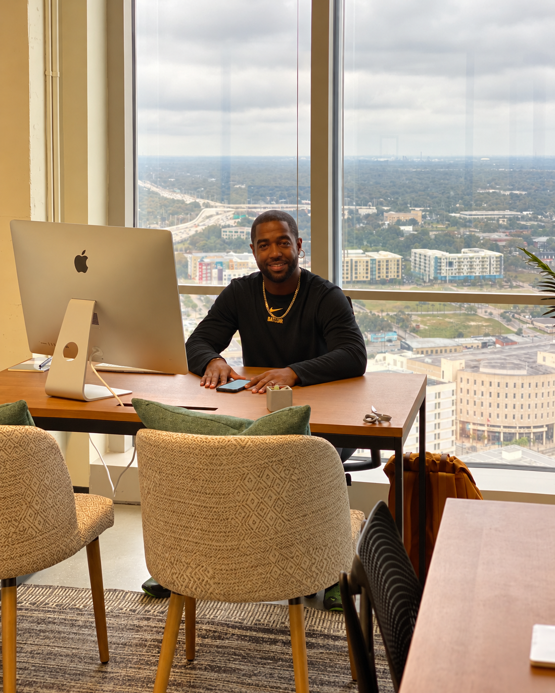 Tony A. Gaskins Jr. seated at his desk in front of tall windows overlooking the city